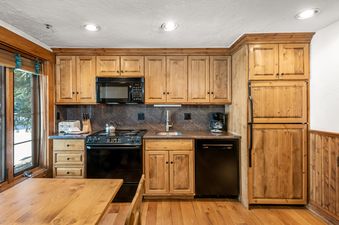 A rustic kitchen with wooden cabinetry, black appliances, and a wooden dining table.