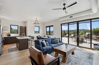 The bright and open living area with a kitchen, dining space, and lounge, featuring a large glass door leading to an outdoor deck with scenic views.
