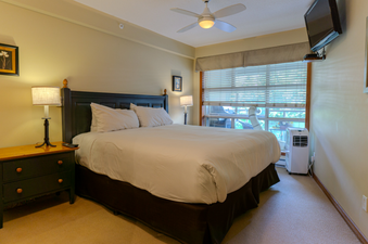 A cozy bedroom featuring a comfortable bed, a ceiling fan, and a view of the outdoors through a large window.