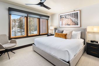 A modern bedroom with a comfortable bed, stylish furnishings, and a large window offering a view of a snowy landscape.