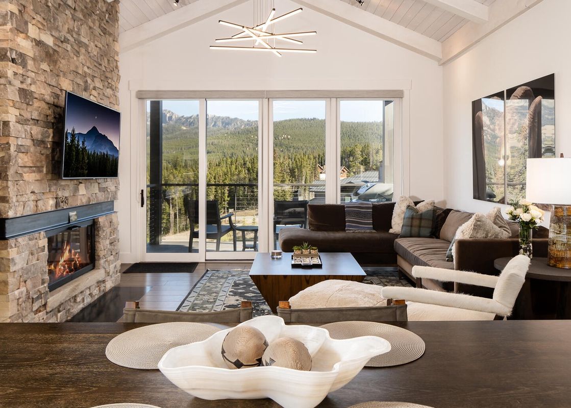 The living room of Moonlight Basin 12 Wildwood, which features a sectional sofa, a fireplace, and a large window with a view of the trees.
