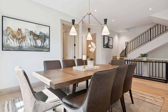 A dining room with a large wooden table and six chairs, featuring a horse-themed painting on the wall and an elegant chandelier hanging above.