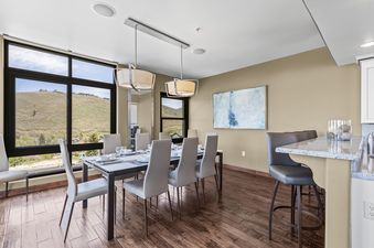 An elegant dining room in Lowell 401 featuring a set dining table with modern pendant lighting and a large window offering expansive views of a green mountain landscape.