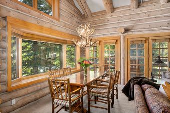 Pine Inn 1 at Trails End Lodge is a spacious cabin featuring a log interior with a large dining room table with 6 chairs and an antler chandelier. It features large windows to enjoy the lush green forest views.
