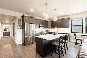 A modern, open-concept kitchen with dark wood cabinets, stainless steel appliances, and a large central island with bar stools.