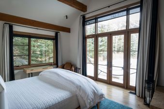 A serene bedroom at Lodge at Shooting Star West 01 with a white bed, a fireplace, and large windows offering a snowy mountain view.