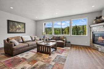 The living room of Pioneer Peak with cozy leather sofas, a rustic coffee table, a colorful area rug, and a fireplace, all set against a stunning mountain view.