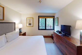 Manor Vail 283 bedroom features a comfortable king bed, a dresser, nightstand with lamp, and a window looking out at the trees.