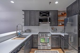 A modern kitchen with dark wood cabinets, stainless steel appliances, and a white countertop, featuring a sink, microwave, and stove.