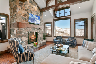 Relaxing living room with a stone fireplace, comfortable furniture, and stunning views of the snow-capped mountains.