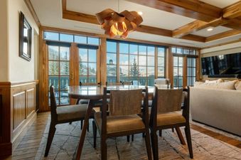 A sophisticated dining area in Chateau Beaver Creek Residence 406 with a circular table, stylish chairs, a unique chandelier, and large windows offering a snowy mountain view.