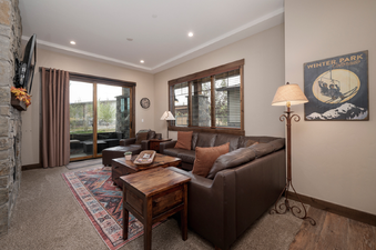 A spacious and inviting living room at Elk Creek Condos B103, featuring comfortable brown leather sofas, a rustic wooden coffee table, and large windows that offer views of the outdoor patio.