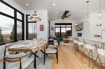 A spacious, modern living and dining area in Frost Haven with large windows, a wooden dining table, comfortable lounge seating, and a stylish kitchen bar with golden stools.