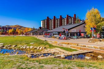 A vibrant autumn day scene captures the Torian Plum Plaza, nestled against a backdrop of mountains ablaze with golden foliage.