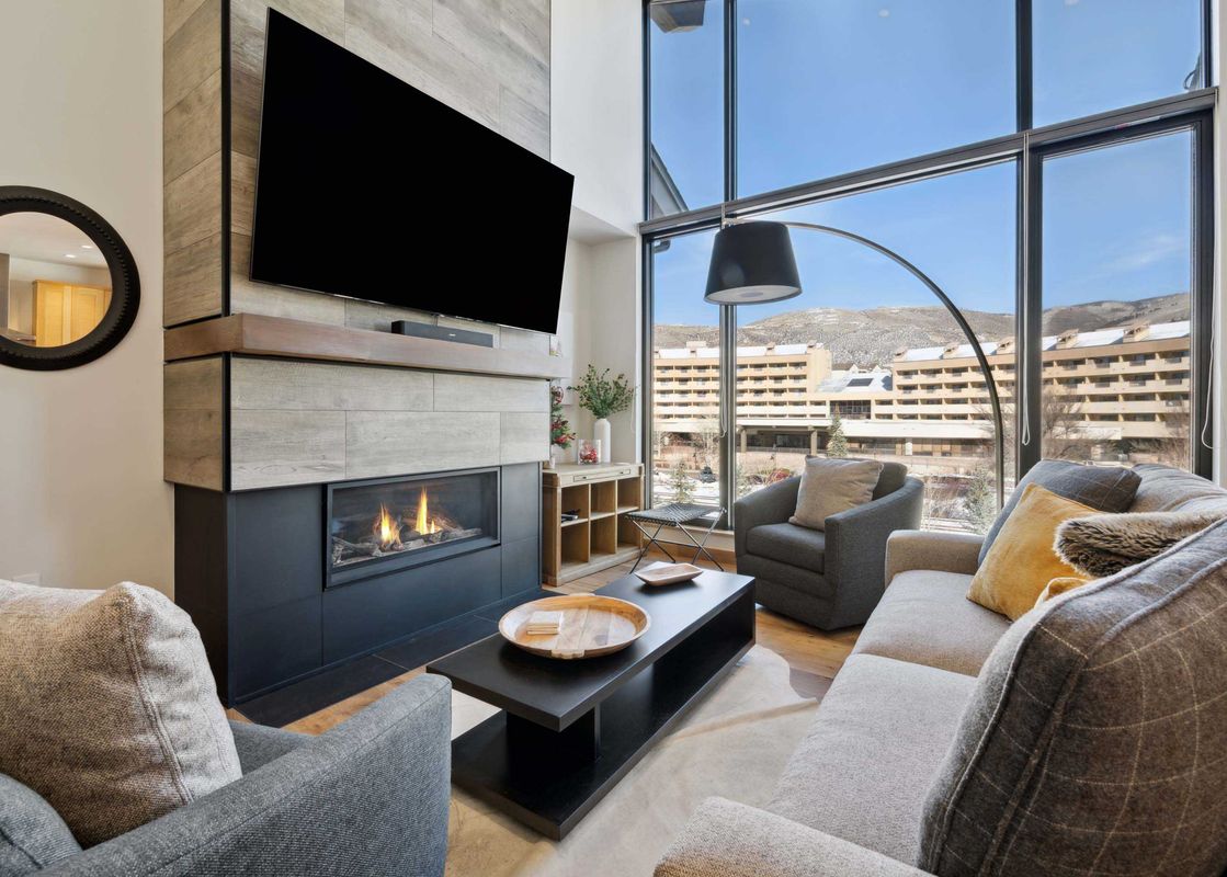 The living room of Riverfront Lodge 401, featuring a gas fireplace, a large flat-screen television, and a comfortable sofa and armchair with views of the mountains.