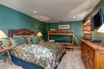 A bedroom in Deer Valley Delight features a king bed with floral bedding, a wooden bunk bed, and a dresser.