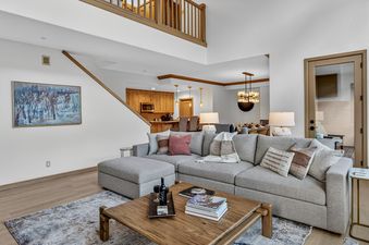 The spacious and inviting living area of the Chalet Bravura with a large sectional sofa, wooden coffee table, and an open-concept layout leading to the dining and kitchen areas.