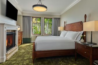 The Montage Deer Valley Resort View Suite features a spacious bedroom with a king-sized bed, a cozy fireplace, and large windows offering views of the surrounding forest.