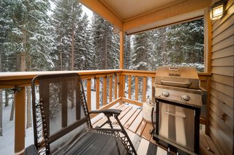 The private balcony at Creekside 403 offers a pristine view of snow-covered pine trees and a convenient BBQ grill, perfect for winter entertaining.