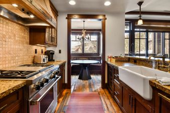 A modern kitchen with wooden cabinetry, granite countertops, and stainless steel appliances is shown, leading to a dining nook with large windows overlooking a snowy landscape.