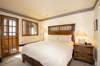 A cozy bedroom with a large wooden bed, two bedside tables with lamps, and a door leading to an outdoor area in Kings Crossing Townhome 4.