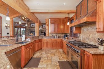 The kitchen at Fox Paw Lodge features a spacious layout with granite countertops, wooden cabinetry, and stainless steel appliances, including a range and dishwasher, set against a backdrop of natural stone and wood accents.