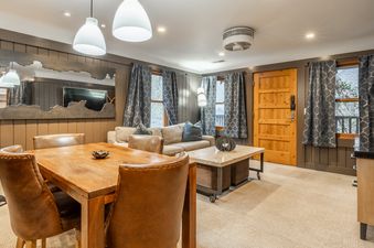 An inviting open-concept living and dining area in Cedar Crest Osprey Cottage 3, featuring a wooden dining table with leather chairs, a comfortable sofa, and tasteful decor under modern lighting.