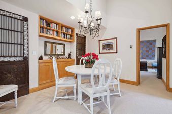 A charming dining area at The Charter E4305 features a round white table, white chairs with floral seats, built-in wooden cabinetry with books, and an elegant chandelier.