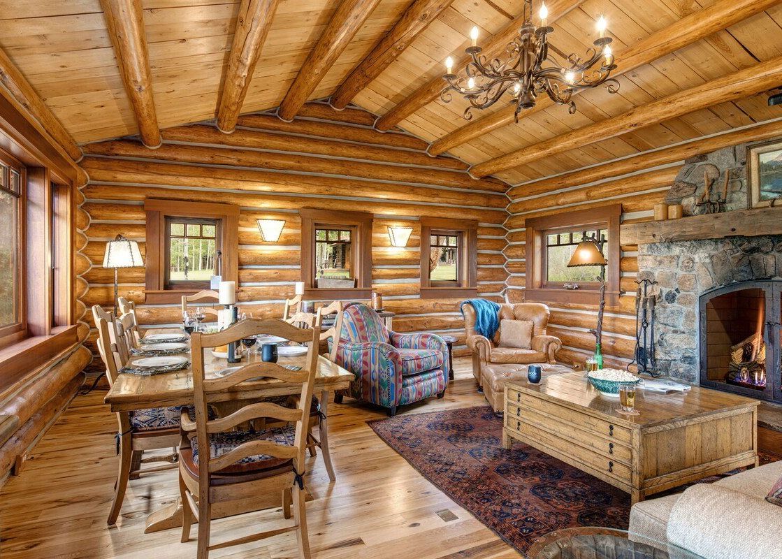 Rustic log cabin living and dining room with a stone fireplace at 7 Cabins Jackson Hole.