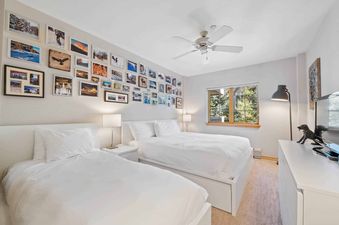 A spacious and brightly lit bedroom at St James Place 325 features two beds with crisp white linens, a window with an exterior view, and a wall adorned with framed photographs.