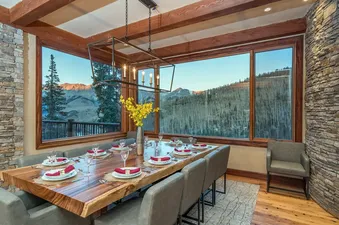 The dining room in Two Trails has a large wood table and chairs, a chandelier, and large windows with a view of the mountains.