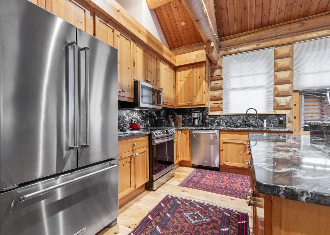 A modern kitchen in Obsidian Jackson Hole, featuring stainless steel appliances, light wood cabinets, and dark marble countertops.
