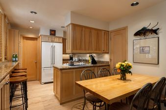 A bright and functional kitchen and dining area in Tamarack 01 with light wood cabinetry, a white refrigerator, and a dining table set with chairs.