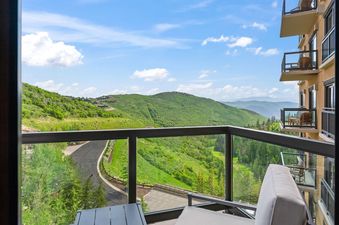The St Regis 2 Bedroom Valley View offers a breathtaking view of lush green mountains under a bright blue sky with scattered clouds, as seen from a private balcony.