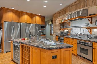 Modern kitchen with stainless steel appliances, a large island with a wine rack, and a stone fireplace.