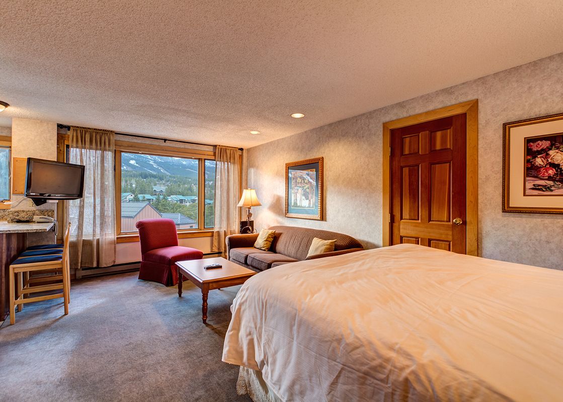 A hotel room with a bed, couch, and a view of the mountains outside the window.