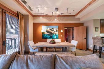 A spacious living room with a large couch, a dining table set with four chairs, and a picture of rocks on the water hanging on the wall.