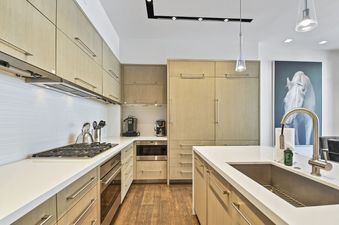 A modern kitchen with light wood cabinets, white countertops, and stainless steel appliances.