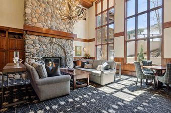 A spacious lounge at Highlands Slopeside 213 features a large stone fireplace, comfortable sofas, and expansive windows with mountain views.