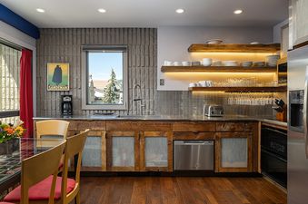 A modern kitchen with wooden cabinetry, stainless steel appliances, and illuminated floating shelves with dishes.