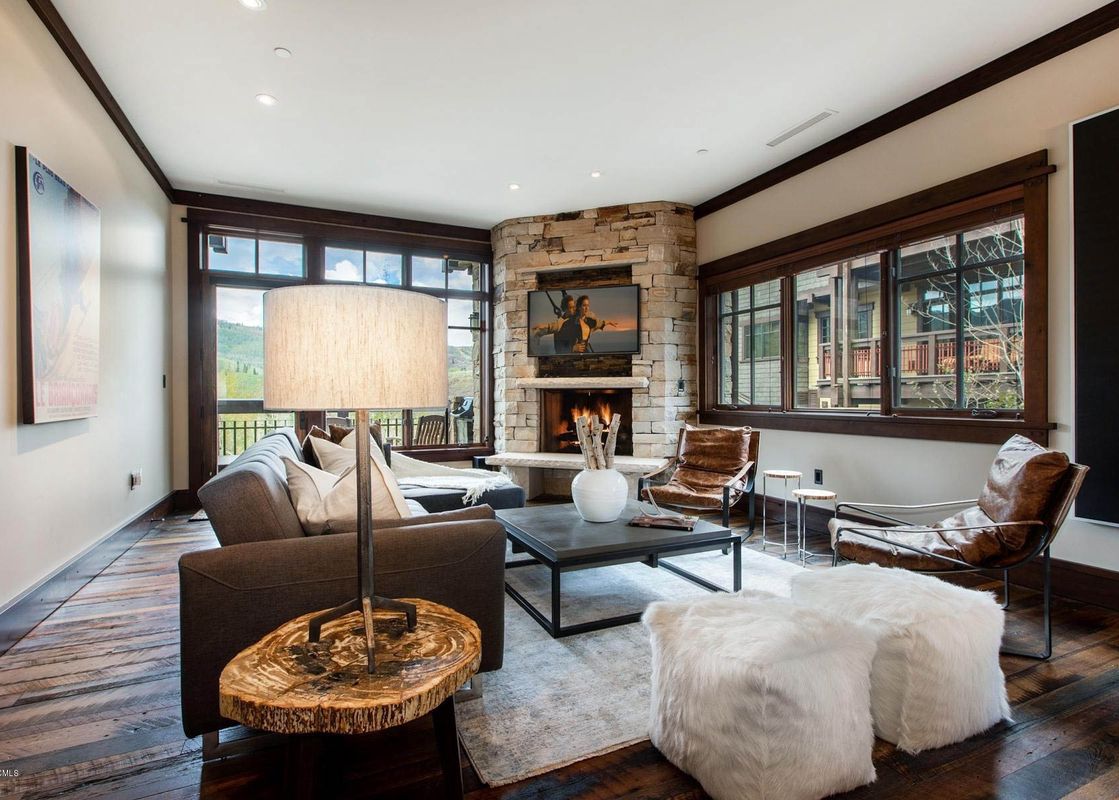 A cozy living room in Arrowleaf Lodge 109 with a stone fireplace, sofa, leather chairs, and large windows offering mountain views.