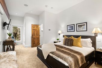 The primary bedroom features a large bed with a dark wooden frame and a cozy fur throw, accompanied by two nightstands with lamps and artwork.