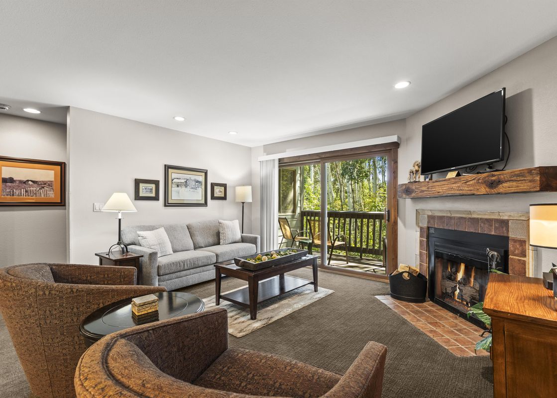 A cozy living room at Snow Flower 142 Park City with a fireplace, comfortable seating, and a balcony with an exterior view.