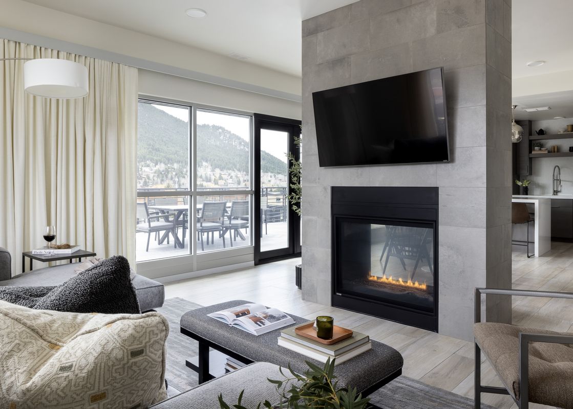 A modern living room with a fireplace, a sectional sofa, and large windows offering a view of snowy mountains.