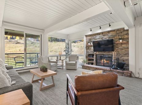 The spacious living room at Enclave 209 features comfortable seating, a stone fireplace with a TV, and large windows with scenic outdoor views.