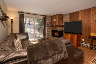 A cozy living room at Beaver Village 211 with a comfortable leather sofa, fireplace, and a large window offering a beautiful snowy view.