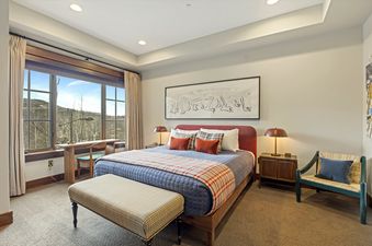A cozy bedroom at The Guardsman Overlook with a king-sized bed, plush bedding, and a large window offering scenic mountain views.