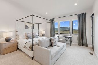 A luxurious master bedroom features a four-poster bed, a sitting area with a sofa, and a dedicated workspace with large windows overlooking a scenic mountain landscape.
