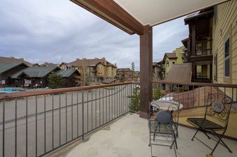 The balcony at Trailhead Lodges 422 features a small table with two chairs, overlooking other buildings in a resort setting under a cloudy sky.