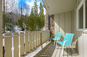 The private balcony offers a serene outdoor space with two chairs, overlooking a snowy landscape with evergreen trees and a bright blue sky.